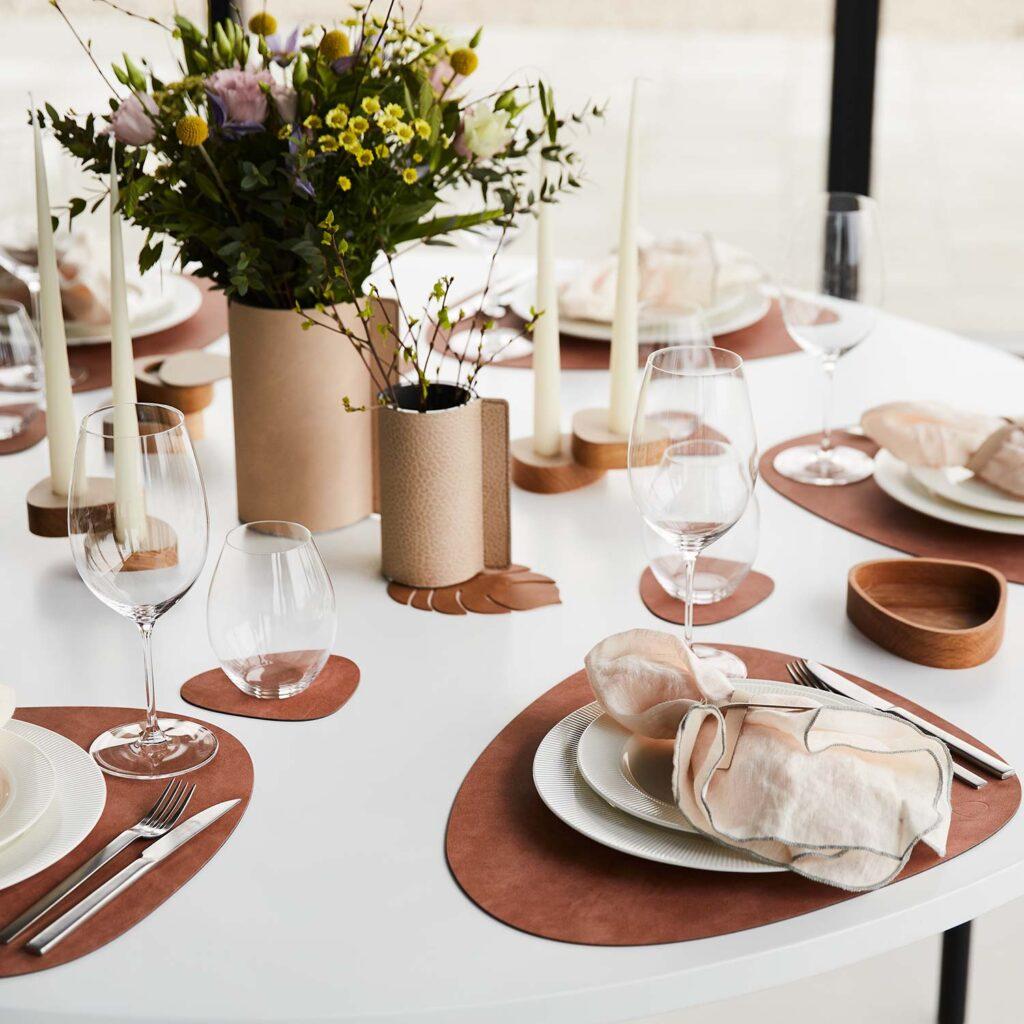 Gedeckter Tisch mit Tischsets aus Leder in Braun, Kerzen und zwei unterschiedlich großen Blumenvasen. Denn moderne Osterdeko ist minimalistisch.
