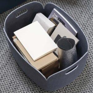 Grauer Muuto Restore Basket aus Filz im Wohnzimmer. Gefüllt mit Büchern und Notizheften.